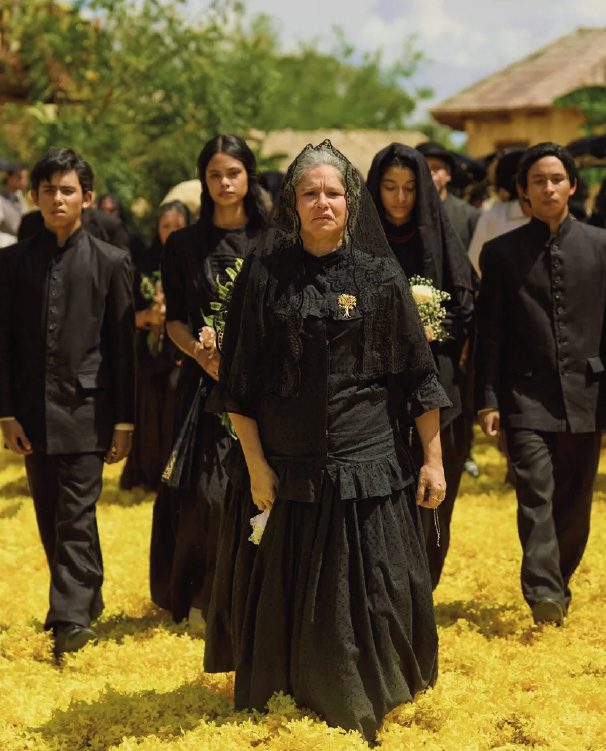 Funeral procession in a rural setting, with an elderly woman dressed in mourning.