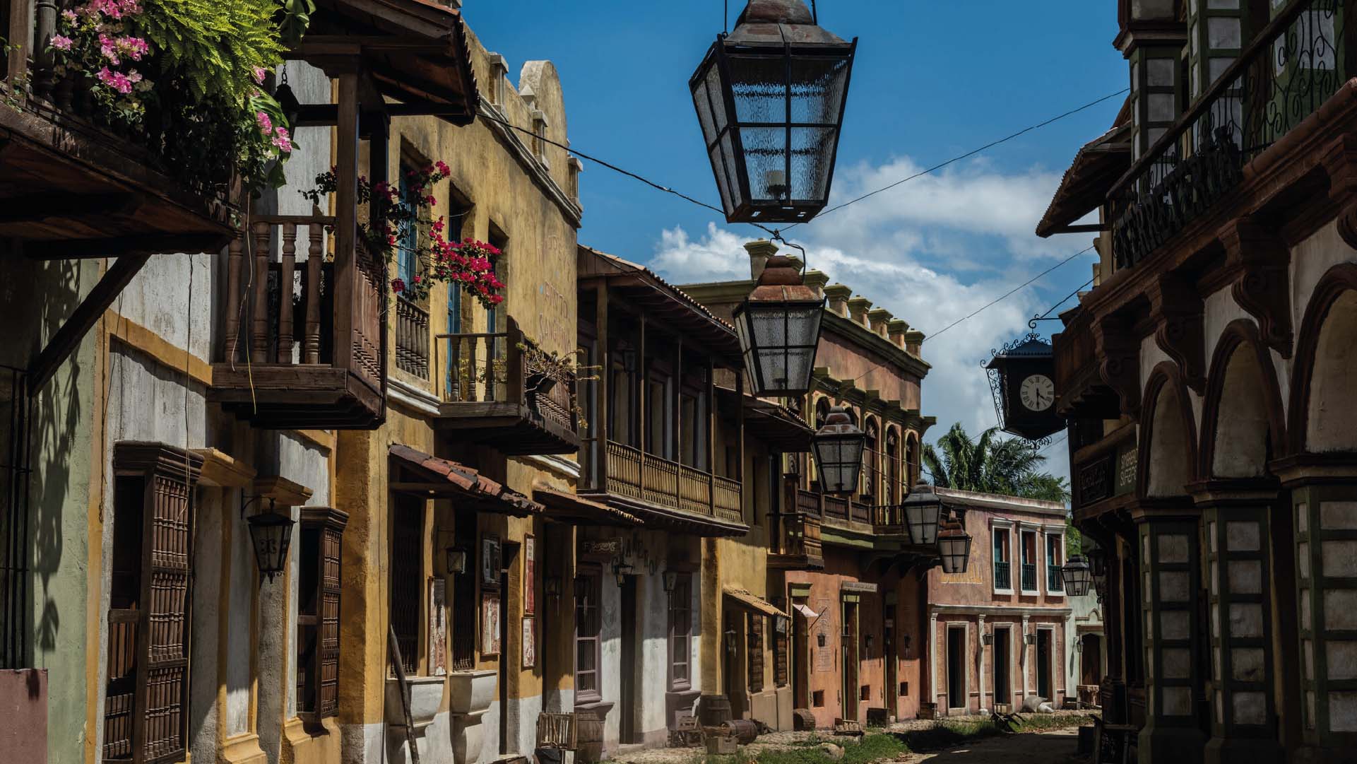 Rue coloniale avec des maisons colorées et des lanternes suspendues.