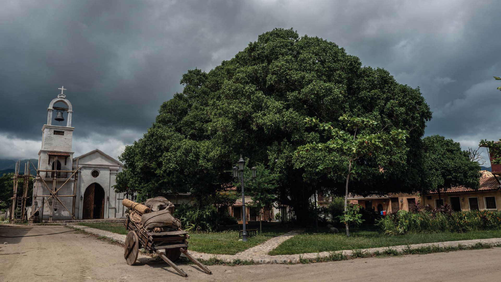 Village with white church, large tree and wooden cart.
