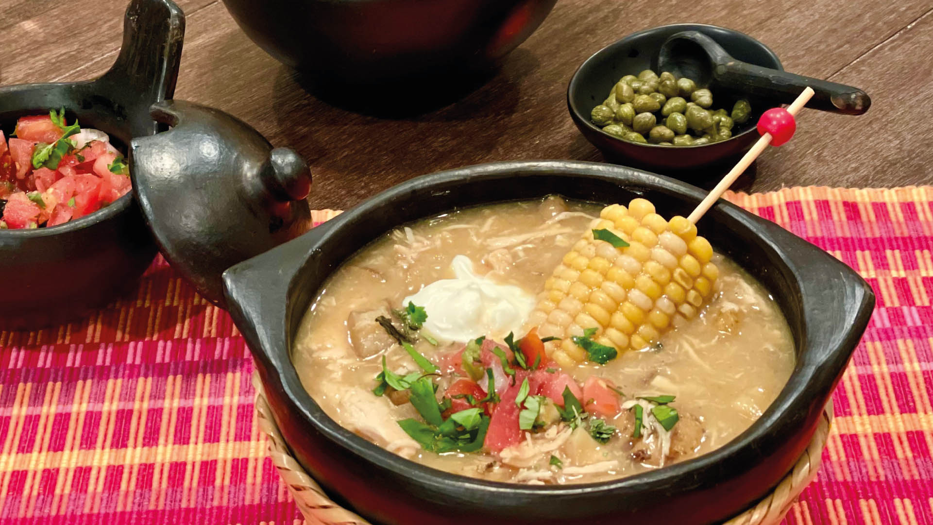 Ajiaco santafereño served in a clay dish with its accompaniments.