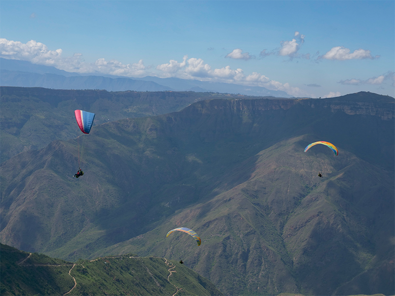Amigos haciendo parapente en el Cañón del Chicamocha, rodeados de imponentes montañas y un cielo azul en Santander – Colombia Travel