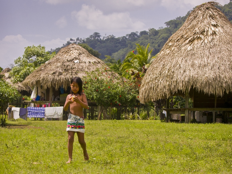 Fotografía de una niña de la comunidad indígena Embera y al fondo cabañas de la aldea en Acandí.