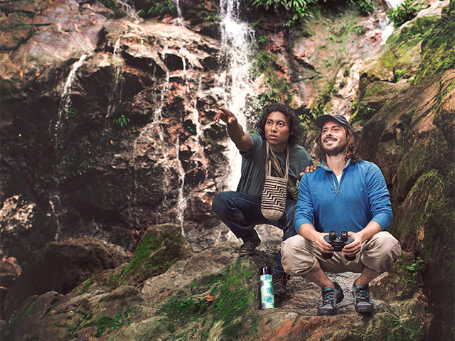 Indigenous guide next to a tourist in front of a waterfall.