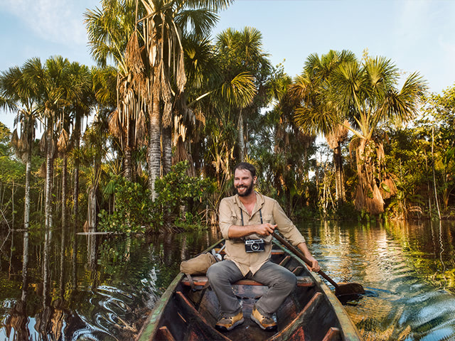 A man dressed as an explorer paddling a canoe in the Amazon.