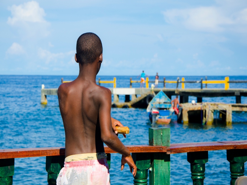 Un joven de espaldas que contempla el bote azul que se reposa en el mar desde el puerto de Acandí.