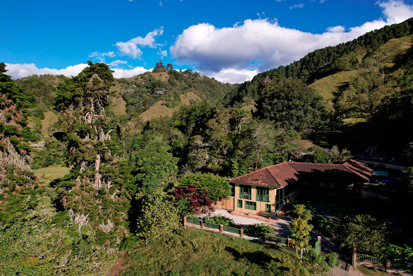 Colonial-style rural house in the middle of a mountainous landscape covered with vegetation.