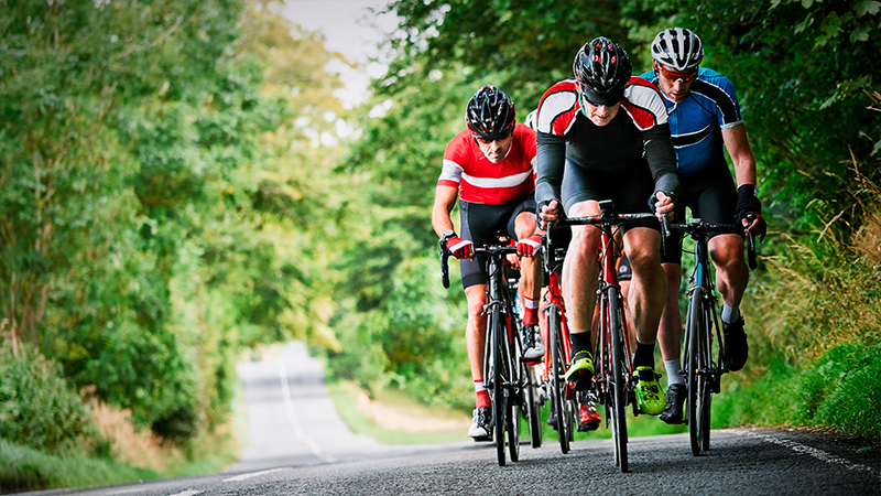 Cyclists running down country lanes on a sunny day while performing during a triathlon training.