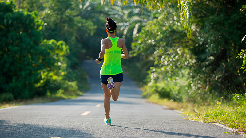 Young gymnast with a bright yellow tank top running on tropical forest trail on a triathlon training.