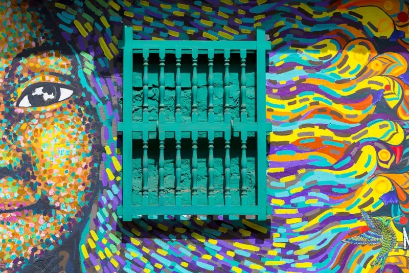 A brightly-colored face painted beside a colonial window