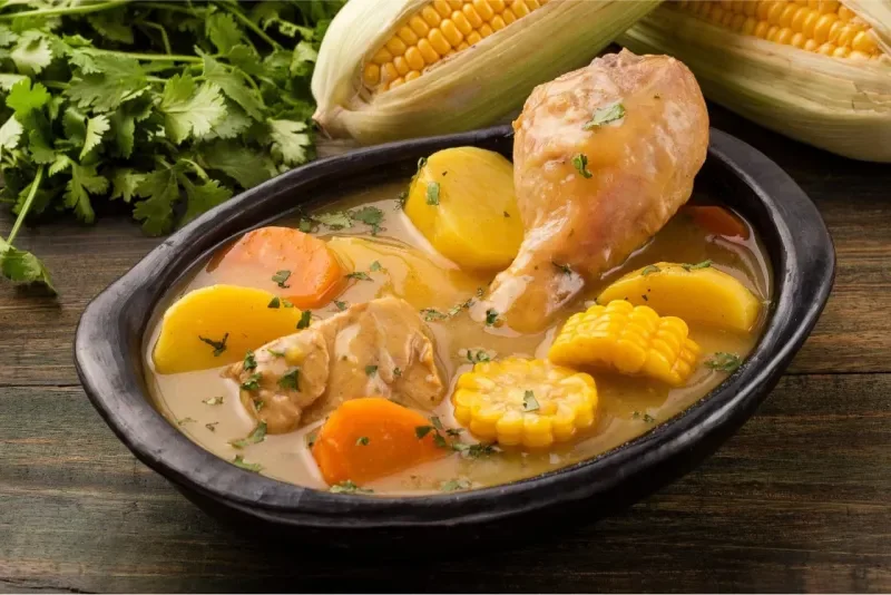 Un plato de Sancocho de pollo servido en un cuenco de cerámica negra sobre una mesa de madera.