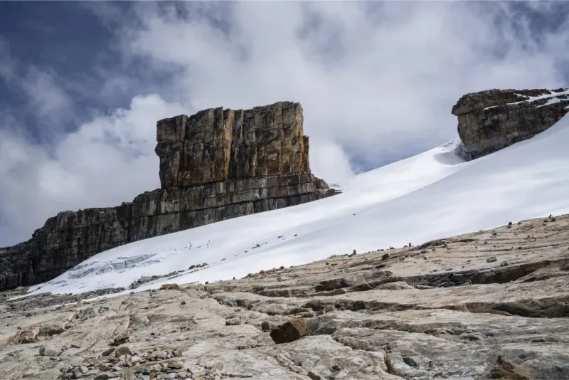 Formación rocosa tabular y escarpada junto a una ladera cubierta de nieve en la Sierra Nevada del Cocuy.