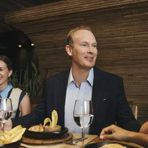 Tres personas sonrientes cenando en un restaurante con decoración de madera y luces tenues.