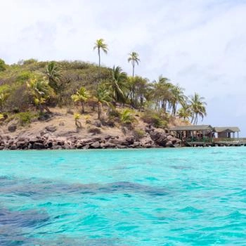 The blue sea of San Andrés with a coast full of vegetation and little wood structures.